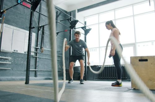 Energetic sportsman is battling ropes working out during sports training with coach young woman in modern gym. Active youth and workout concept.